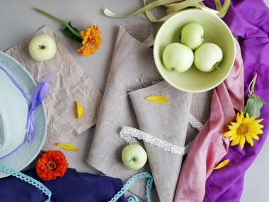 Elma, sarı yaprakları, yeşil şapka ve hafif bir arka plan gri tuval ve pembe ve mor bez, taze çiçekler görünümü top. Mevsimlik dekoratif kompozisyon, natürmort. Yaz, sonbahar