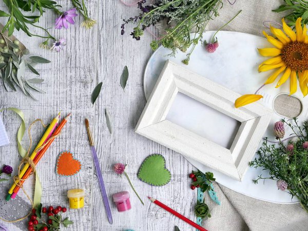 Сезонный декоративный состав цветов, ягод, художественных и канцелярских материалов, сердца из войлока на фоне светлой древесины, вид сверху. Поздравляем с праздником
