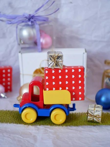 Toy bright car, boxes with gifts, Christmas decorations, New Year\'s decor, balls on a light background, concept of congratulations on seasonal winter holidays, Christmas, New Year, home interior