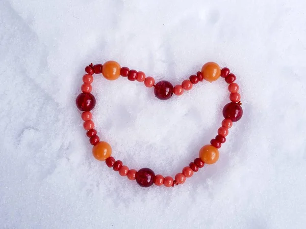 红色和橙色的珠子以一颗心的形状布置在雪地里 顶视图 冬天的概念季节性浪漫的问候 情人节的象征 — 图库照片