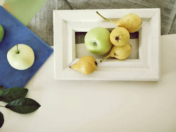 Yellow pears and apples in a white wooden frame, leaves, seasonal summer composition on a light background, top view, the concept of a healthy lifestyle