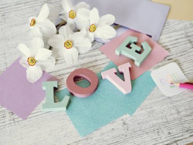  Anneler günü tatili, toplu harflerden aşk kelimesinin kompozisyonu, taze çiçekler, zarf, kağıt, masanın üzerinde kalemler, üst görünüm