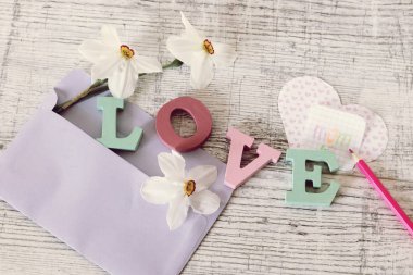  Anneler günü tatili, toplu harflerden aşk kelimesinin kompozisyonu, taze çiçekler, zarf, kağıt, masanın üzerinde kalemler, üst görünüm