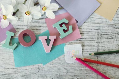 Anneler günü tatili, toplu harflerden aşk kelimesinin kompozisyonu, taze çiçekler, zarf, kağıt, masanın üzerinde kalemler, üst görünüm