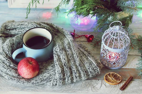 Büyük bir fincan kahve, bir elma, Noel dekorlu ahşap bir masanın üzerine örme yünlü bir eşarp, yanan mumlar, köknar dalları, ev konforunda mevsimlik kış tatilleri