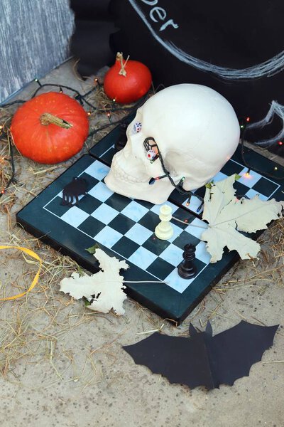 Хэллоуинская композиция черепов, осенних листьев, подсветки, мистический декор на шахматной доске и бетонная поверхность на черном фоне
