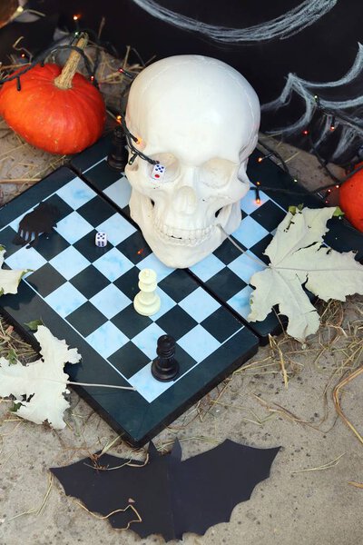 Хэллоуинская композиция черепов, осенних листьев, подсветки, мистический декор на шахматной доске и бетонная поверхность на черном фоне
