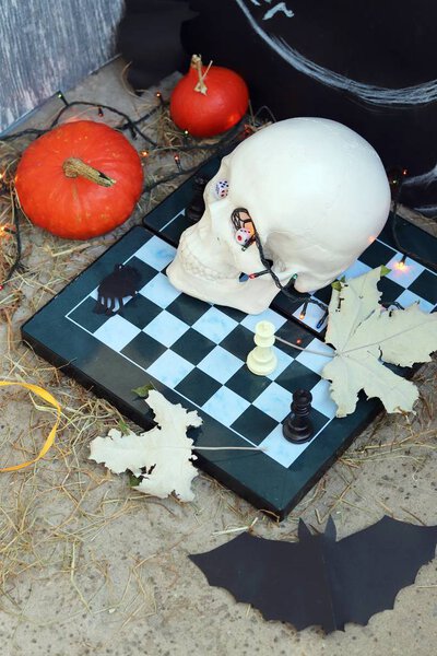 Хэллоуинская композиция черепов, осенних листьев, подсветки, мистический декор на шахматной доске и бетонная поверхность на черном фоне
