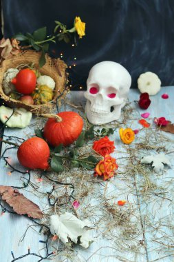 Taklit kafatası, kabaklar, taze güller, saman, yaprakları ve sonbahar yaprakları ile serpiştirilmiş ahşap bir yüzey üzerinde aydınlatma ışıkları yapılmış Halloween dekoratif kompozisyon