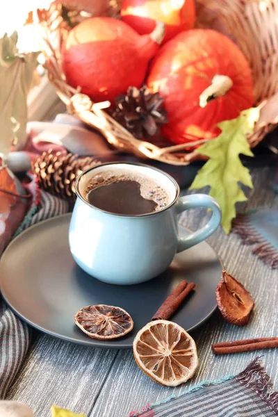 Cup of coffee, pumpkins, leaves, spices, a scarf on a wooden surface on a window background, home comfort concept, Thanksgiving, autumn season