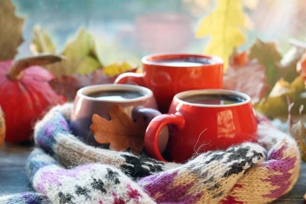 Üç fincan kahve, balkabağı, yapraklar, arka planda yün bir eşarp, ev konforu, aile, Şükran Günü, sonbahar sezonu