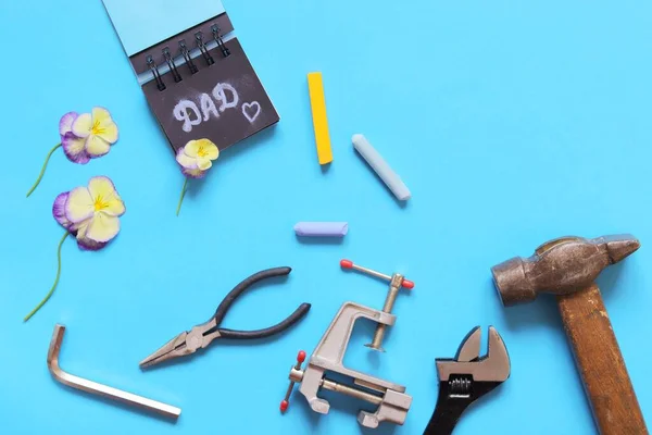 Father's day, tools, inscription dad, flower on wooden background, holiday greetings concept