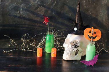 Kafatası, oyuncak örümcekler, yeşil kokteylli şişeler, siyah ahşap bir masa üzerindeki aydınlatma, bayram için iç mekan, mistik dekor, Ekim