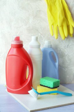 Plastik şişelerde, süngerlerde ve fırçalarda sıvı deterjanlar, ev temizliği ve temizlik için lastik eldivenler ahşap bir masada, ev teslimatı.