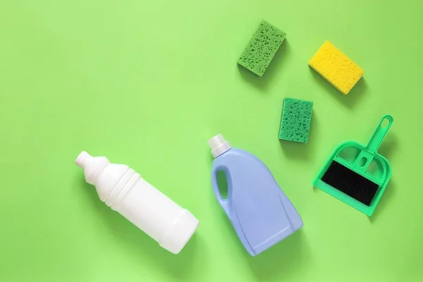 Plastik şişelerdeki sıvı deterjanlar, fırçalar ve süngerler parlak yeşil bir arka planda evi temizlemek için.