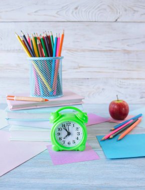 Okul konseptine geri dönelim. Çalar saat, kitap yığını, elma, renkli kalemler ve beyaz ahşap arka planda pastel renkli kağıt..