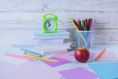 Okul konseptine geri dönelim. Çalar saat, kitap yığını, elma, renkli kalemler ve beyaz ahşap arka planda pastel renkli kağıt..
