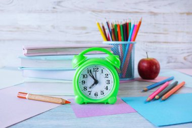 Okul konseptine geri dönelim. Çalar saat, kitap yığını, elma, renkli kalemler ve beyaz ahşap arka planda pastel renkli kağıt..
