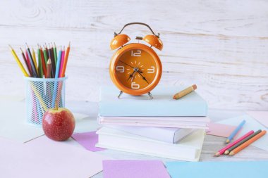 Okul konseptine geri dönelim. Çalar saat, kitap yığını, elma, renkli kalemler ve beyaz ahşap arka planda pastel renkli kağıt..
