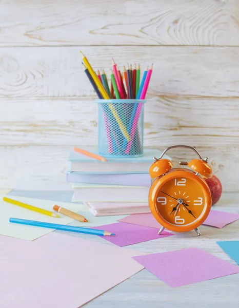 Okul konseptine geri dönelim. Çalar saat, kitap yığını, elma, renkli kalemler ve beyaz ahşap arka planda pastel renkli kağıt..