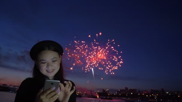 Fuegos artificiales y chica feliz usando el teléfono en el terraplén — Vídeos de Stock