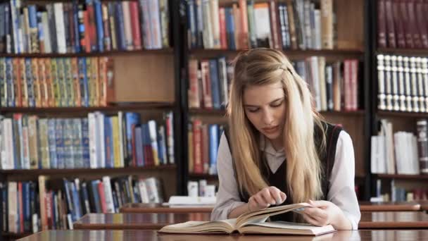 Красива студентка читає книгу в бібліотеці — стокове відео