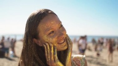 Yetişkin trendy genç kız ile kaplı altın parlak plaj kameraya poz yüzüne. Güneşli hava, güneş ışınları sparkles üzerinde oynanır. Yaz aylarında, istirahat, modelleme ve sanat kavramı