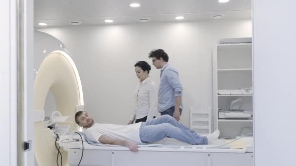 Доктор контролінг як медсестра поставити навушники для пацієнта голови перед МРТ — стокове відео