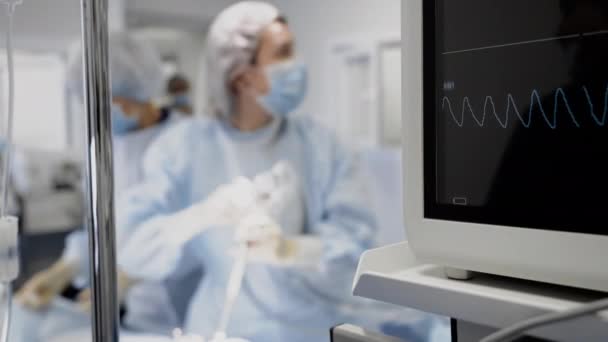 Kardiogram a monitor képernyőjén, és sebész orvosok a működési szobában a háttérben — Stock videók