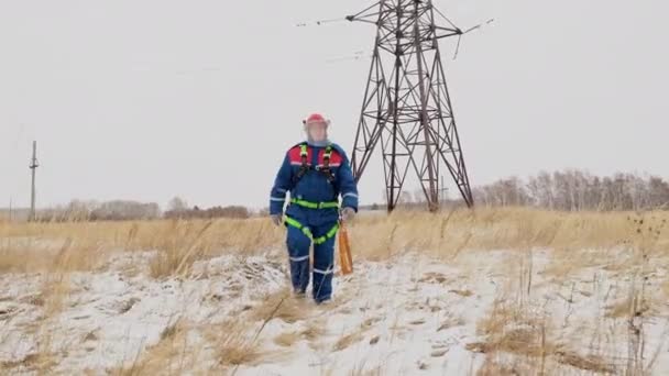 Müder Reparaturmann läuft mit Elektrizitätswerk über das Winterfeld — Stockvideo