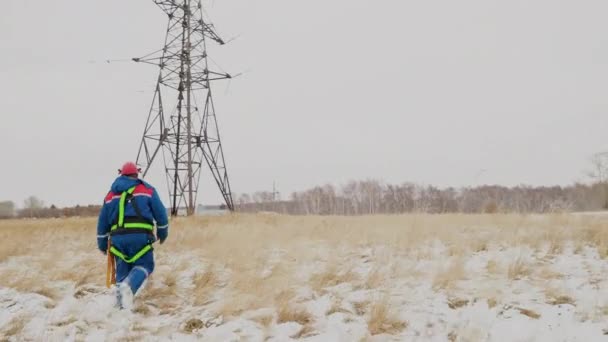 Чоловік йде до електричної вежі на енергетичній станції на зимовому полі — стокове відео