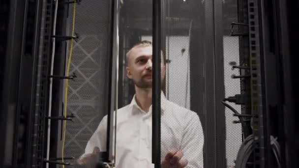 IT-инженер, работающий с ноутбуком перед открытием серверной стойки в комнате — стоковое видео