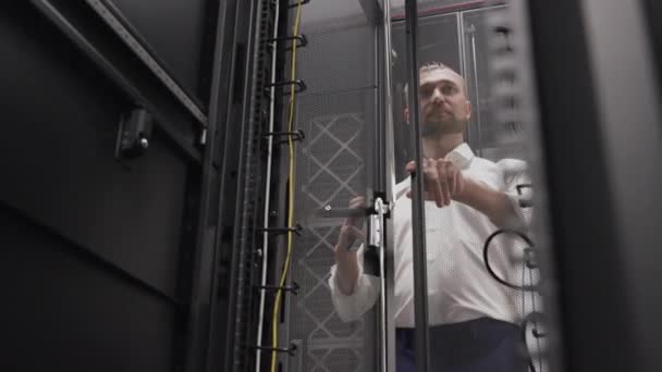 Человек открывает серверную стойку хостинга в большом дата-центре — стоковое видео