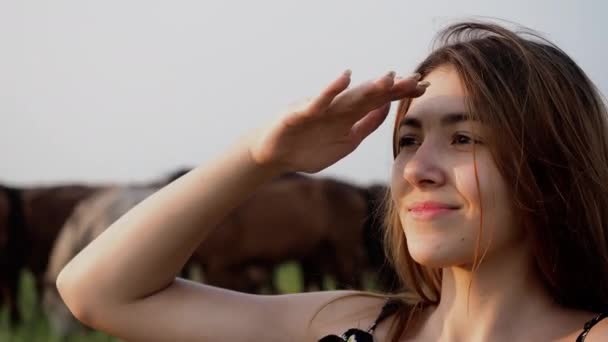 Menina sorridente feliz olhando para o pôr do sol com o rebanho de cavalo no fundo — Vídeo de Stock