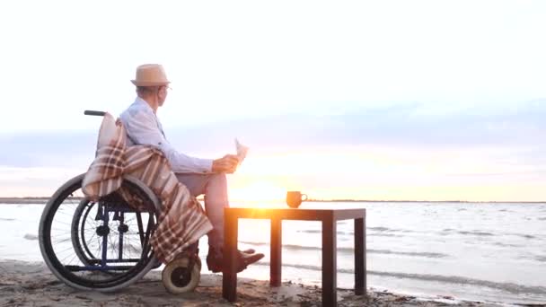 Uomo disabile, handicappato vecchio nonno legge giornale seduto in sedia a rotelle — Video Stock