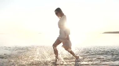 Genç mutlu kız deniz suyuna su sıçratır, kaygısız, ferahlatıcı, dinlendirici yürüyüşün tadını çıkarır.