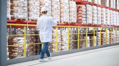 Elinde evrakları olan bir işçi büyük bir depoda raflarda elinde kutularla dolaşıyor ve malların bulunup bulunmadığını kontrol ediyor. Hızlı büyüyen e-ticaret endüstrisindeki modern dağıtım merkezi