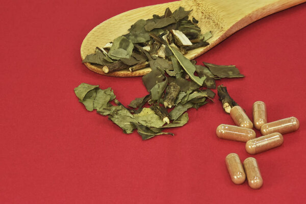 Зеленый чайный лист и капсула подаются в деревянной ложке из бамбука на красном фоне
.