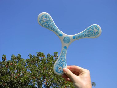 Man's hand with plastic boomerang read to flight on a blue sky. clipart