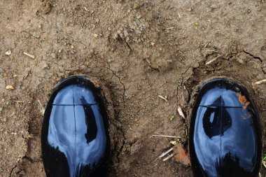 Çıplak araziye basan kişi. Kırsal alanda yürümek için güvenlik botu. Siyah plastik kir çizme.