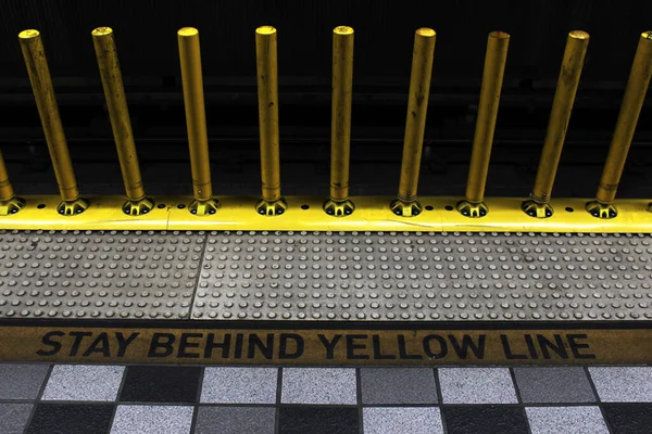 Sarı çizginin gerisinde kalın. Metro uyarı işaretleri ve metro istasyonunda sarı güvenlik direkleri. Metro platformu..