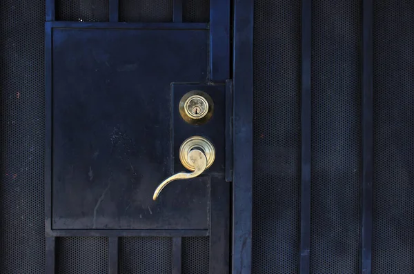 Gold-plated metal door handle on a black iron door with a grille. Door handle with lock on closed door.