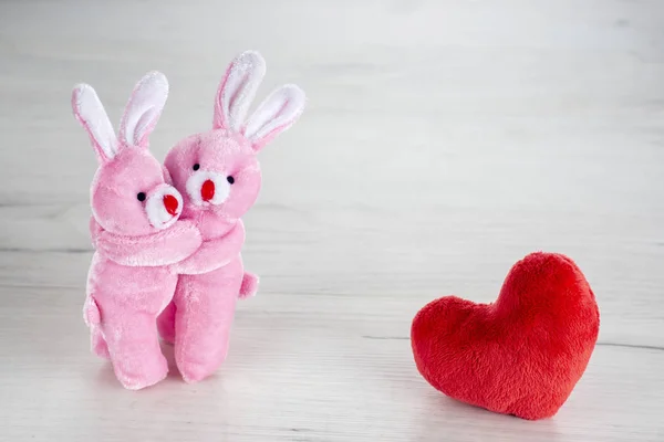 粉红玩具兔子拥抱在红色毛绒的心脏附近 — 图库照片