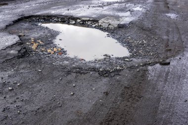 Çukur ve su birikintisi olan kötü asfalt yol