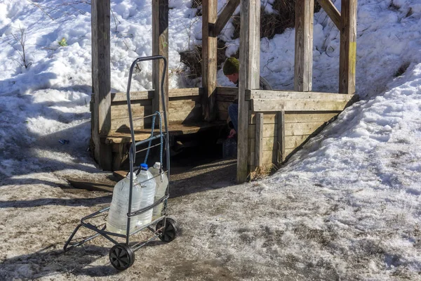 City dweller collects clean spring water from natural spring into empty cans