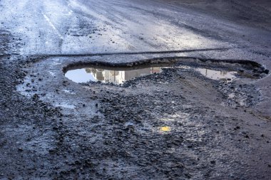 Büyük bir çukur ve su birikintisi ile şehir caddesinde asfalt yol