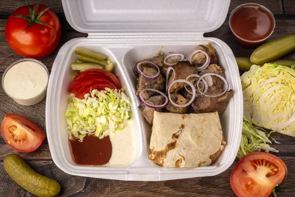 Takeaway fast food in lunch box - fresh vegetables, pita bread and pork