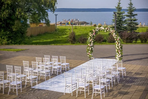 Wedding place on lakeside with arch of flowers and white chairs