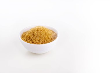 Beyaz arka planda beyaz kasede kahverengi doğal kamış şekeri.