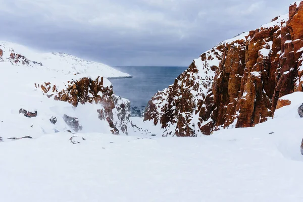 高の赤い岩は北極に遠征中に不気味な寒さと強い風で冬の海の雪に覆われた海岸を超えて上昇します — ストック写真